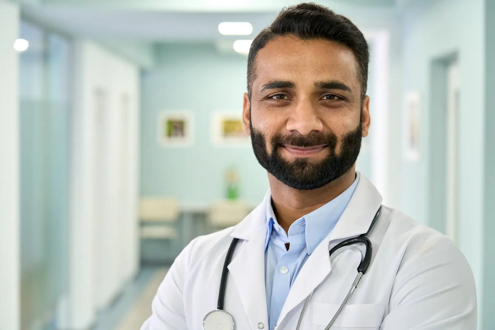 Smiling bearded male Indian doctor wearing medical coat looking at camera. Headshot portrait of ethnic hispanic man medic professional, hospital physician, confident practitioner or surgeon at work.